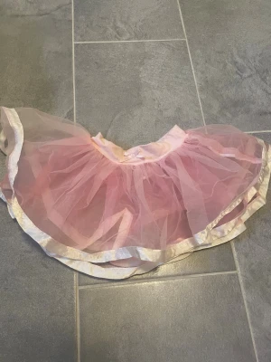 Rosa tyllkjol med volangkant - Söt rosa kortkjol i tyll med volang och glansig ljus kant. Kjolen har ett fluffigt utseende och resår i midjan för bekväm passform. Perfekt för dig som vill ha en lekfull och drömmig stil.