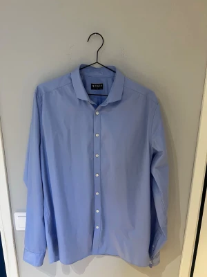 Ljusblå skjorta från Tiger of Sweden - Säljer en stilren ljusblå skjorta från Tiger of Sweden i slim fit. Skjortan har klassisk krage, långa ärmar och vita knappar framtill. Perfekt för dig som gillar en clean och enkel look.