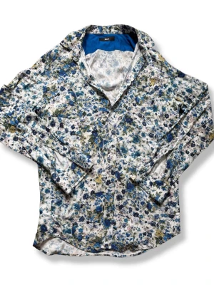 Blommig skjorta från Diesel - Säljer en blommig skjorta från Diesel i vitt med blå, gröna och gula toner. Skjortan har lång ärm, klassisk krage och knäppning framtill. Perfekt för dig som vill sticka ut med ett färgglatt mönster och skön bomullskänsla.
