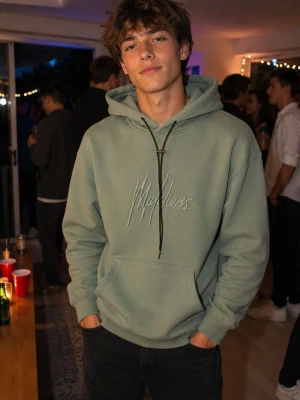 Grön hoodie med broderad text 100% bomull - Snygg grön hoodie med broderad text på bröstet i vitt. Hoodien har en stor känguruficka framtill, ribbade muddar och justerbar huva med svarta snören. Perfekt för en chill och avslappnad stil.