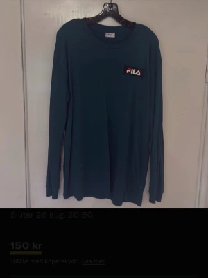 Mörkgrön långärmad topp från FILA - Snygg mörkgrön långärmad topp från FILA med tryckt logga på bröstet och stort grafiskt tryck på ryggen. Perfekt för dig som gillar sportig och avslappnad stil. Tillverkad i mjukt material som känns skönt mot huden.