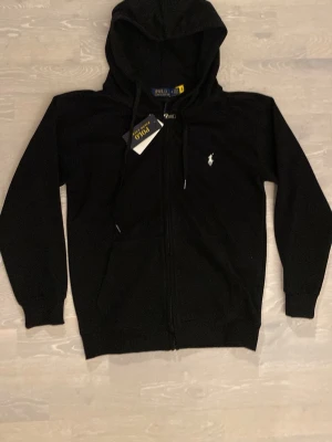 Svart hoodie från Polo Ralph Lauren - Tja säljer en Snygg svart hoodie från Polo Ralph Lauren med dragkedja framtill och klassisk vit logga på bröstet.  Storlek är S och den är i helt nytt skick. Priset kan diskuteras och skickar inom 24 Tim