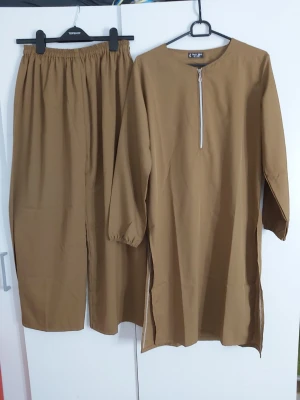 Beige långärmad topp med dragkedja och vidben byxor - Snygg beige långärmad topp med rund halsringning och dragkedja framtill. Toppen har slitsar på sidorna och är gjord i ett mjukt material som känns skönt mot huden. Perfekt för dig som gillar en enkel men stilren look.
