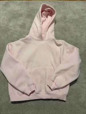 Ljusrosa hoodie  - Säljer en ljusrosa hoodie i storlek XS. Tröjan har en stor huva, ribbade muddar och en klassisk magficka. Materialet är mjukt och fleecigt på insidan, perfekt för att chilla eller hänga med kompisar.