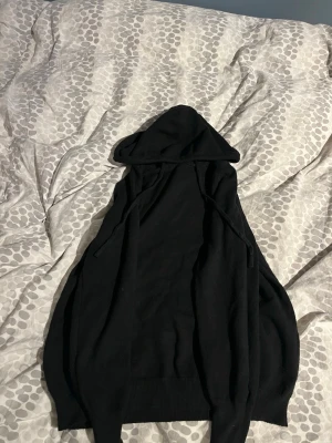 Stickad merinoull hoodie  - Säljer en svart hoodie med huva och Hoodien har en klassisk passform och är tillverkad i ett mjukt, stickat material som känns skönt mot huden. Perfekt för dig som gillar en enkel och clean stil.
