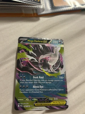Mega Darkrai EX Pokémonkort - Unikt Mega Darkrai EX Pokémonkort med holografisk effekt och färgstarka detaljer i svart, lila och grönt. Kortet har 280 HP och attacker som Dusk Raid och Abyss Eye. Perfekt för samlare eller Pokémonfans som vill utöka sin samling.
