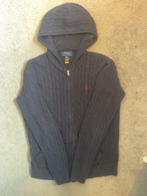 Kabelstickad RL tröja säljes ev bytes! - Mörkblå kabelstickad zip hoodie från Polo Ralph lauren. Verkligen ett fint plagg med perfekt passform. Storlek 14-16 men passar mig som är 176 cm lång perfekt. Har tyvärr ej kvar kvittot. Jag tar även byten med liknande värde!  Nypris 1800kr säljes för 1000 kr billigare!