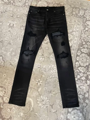 Svarta ripped jeans - Säljer ett par svarta skinny jeans från miri med slitningar och hål på både fram- och baksida. Jeansen har klassisk femficksmodell, knappgylf och är tillverkade i stretchigt denimtyg för en bekväm passform. Perfekta för en edgy streetstyle-look.