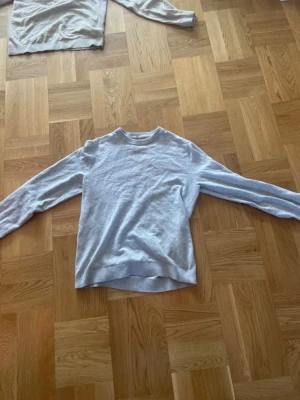 Grå tröja från Jack & Jones - En stilren ljusgrå tröja från Jack & Jones med rund halsringning och ribbade muddar. Perfekt basplagg till garderoben, enkel att matcha och skön att bära. Tillverkad i mjukt material för extra komfort.