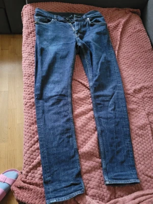 Mörkblå jeans från Tiger of Sweden - Säljer ett par mörkblå jeans från Tiger of Sweden med slim passform. Jeansen har klassisk femficksdesign, dragkedja och är tillverkade i bomull. Snygga kontrastsömmar och stilren look som funkar till det mesta.