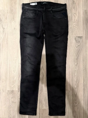 Replay Anbass Hyperflex Jeans Svarta W31/L32 - Slim Fit - Replay Anbass Hyperflex svarta jeans i stretchig Hyperflex denim med slim fit passform som sitter snyggt och bekvämt och funkar till allt, storlek W31/L32, midja 41,5 cm, ytterbenslängd 102,5 cm, benöppning 15 cm, modellen är 185cm & väger 65kg, i fint skick.
