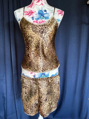 Leopardmönstrat set med linne och shorts - Snyggt set med linne och shorts i leopardmönster. Tunt, glansigt material med smala axelband på linnet och avslappnad passform på shortsen. Perfekt för dig som gillar djurmönster och vill sticka ut.