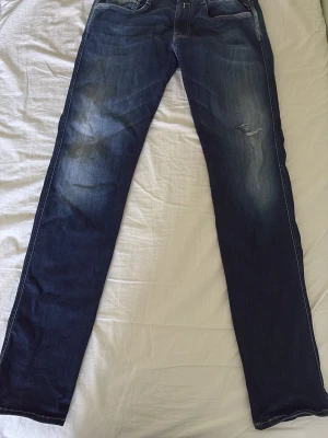 Mörkblå raka jeans med slitningar - Säljer ett par mörkblå replay jeans med raka ben och snygga slitningar på framsidan. Jeansen har klassisk femficksdesign och kontrastsömmar. Materialet är denim i bomull och passformen är slim fit men ändå stilren. Model Anbass