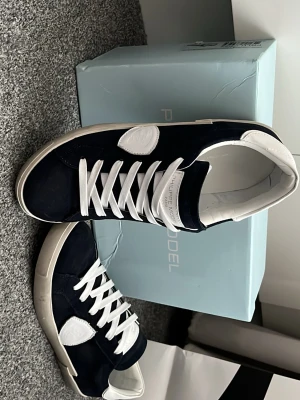 Philippe Model blåa sneakers - Snygga blåa sneakers från Philippe Model med vita detaljer och vita skosnören. Skorna har en klassisk låg siluett och är tillverkade i mocka och läder. Ikonisk logotyp på sidan och bekväm innersula. Perfekta för en trendig streetwear-look. Priset går såklart att diskuteras vid affär.😁