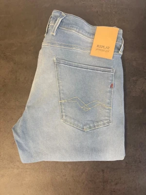 Ljusblå Replay Hyperflex jeans, stl 33/32 - Säljer ett par ljusblå jeans från Replay Hyperflex med klassisk femficksmodell och raka ben. Jeansen har snygga sömdetaljer på bakfickan och är tillverkade i stretchigt denimtyg för extra komfort. Perfekta för en avslappnad och trendig look.