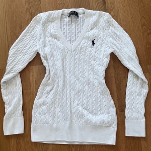 Vit kabelstickad tröja Polo Ralph Lauren - Kabelstickad vit tröja från Polo Ralph Lauren med djup V-ringning och marinblå broderad logga på bröstet. Köptes för 2 200kr, hör av er vid frågor eller mer🤍