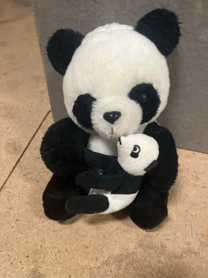 Mjukisdjur panda med unge - Söt mjukispanda i svart och vitt som håller en liten pandaunge i famnen. Tillverkad i mjukt plyschmaterial och har broderade detaljer på nos och ögon. Perfekt som present eller dekoration.