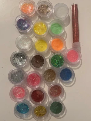 Färgglada glitter och flakes för naglar - Säljer ett stort set med glitter och flakes i olika färger för nageldekoration. Perfekt för att skapa unika och kreativa nageldesigner. Innehåller bland annat rosa, blått, grönt, gult, orange, silver och guld glitter i små burkar samt en tub med kopparfärgat glitter.