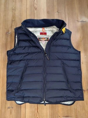Mörkblå dunväst från Parajumpers XXL - Snygg mörkblå dunväst från Parajumpers i storlek XXL. Västen har quiltad design, dragkedja framtill och två snedställda fickor med dragkedja. Lättviktig och perfekt för lager-på-lager. Klassisk look med gul detalj vid kragen. Aldrig använd utan bara hängt i garderoben så jag köpt den för stor!      Nypris:4154kr.    Mitt pris: 2115kr
