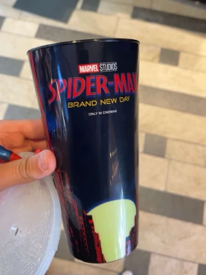 Spider-Man mugg med figur och lock - Cool svart plastmugg med Spider-Man Brand New Day-tryck från Marvel Studios. Muggen har ett stadsmotiv och ett genomskinligt lock. På locket sitter en 3D-figur av Spider-Man som hänger upp och ner. Perfekt för Marvel-fans!