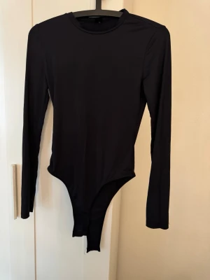 Svart långärmad body från SHEIN - En stilren svart body från SHEIN med långa ärmar och rund halsringning. Tillverkad i ett stretchigt och mjukt material som sitter tajt mot kroppen. Perfekt att matcha med jeans eller kjol för en clean look.