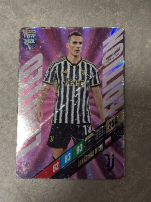 FIFA 365 Panini fotbollssamlarkort - Säljer ett FIFA 365 Panini Adrenalyn XL samlarkort med fotbollsspelaren Arkadiusz Milik från Juventus. Kortet har lila och guld bakgrund med holografiska detaljer och spelarstatistik på framsidan. Perfekt för dig som samlar på fotbollskort.
