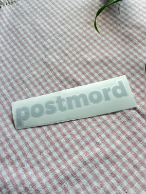 Postmord dekal bil / EPA Vit klistermärke med texten postmord - Säljer ett vitt klistermärke med texten 'postmord' i rundad font. Perfekt för att sätta på laptop, cykel, bil, EPA, eller anteckningsbok. Tillverkad i plastmaterial och enkel att applicera på släta ytor.