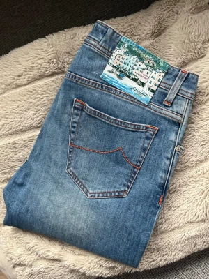 Jacob Cohen Portofino - Säljer ett par klassiska Jacob Cohen Portofino jeans med snygga orange kontrastsömmar och fem fickor. Jeansen har en rak passform och är tillverkade i denim. Perfekta för en avslappnad och trendig look.