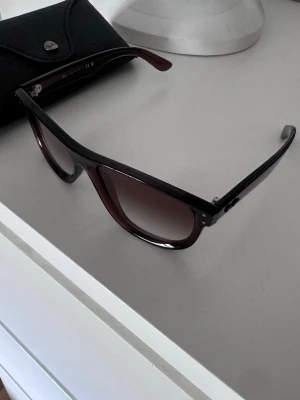 Svarta Ray-Ban Boyfriend Reverse solglasögon - Säljer ett par Ray-Ban Boyfriend Reverse solglasögon med svart båge och mörka glas. Klassisk och stilren design med rektangulär form. Kommer med originalfodral. Perfekta för dig som vill ha en tidlös accessoar till sommaren.