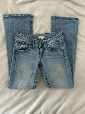 Ljusblå bootcut jeans med dubbla knappar - Snygga ljusblå bootcut jeans med dubbla knappar i midjan och klassiska fem fickor. Jeansen har en lätt tvättad look och raka, utsvängda ben. Jeans från Ginatrico YOUNG i storlek 152 cm. Använda fåtal gånger.