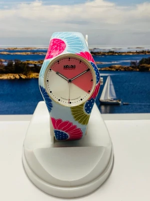 Färgstark Kolor by Noon Copenuhagen damklocka  - Färgstark Kolor by Noon Copenuhagen damklocka med ett unikt blommigt mönster på boetten och armbandet. Urtavlan har en distinkt design med vita och rosa sektioner. Klockan drivs av ett kvartsurverk och har ett armband i silikon. Baksidan av boetten är märkt med "KOLOR by noon copenhagen" och "01-047-46". Klockan har nytt batteri och säljes i befintligt skick enligt bilderna! 