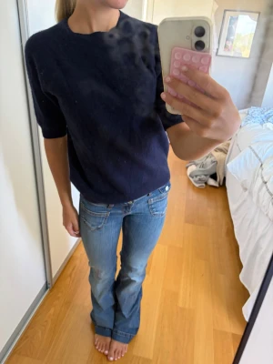 Mörkblå stickad tröja med kort ärm - En enkel och stilren mörkblå stickad tröja med korta ärmar och rund hals. Tröjan har en rak passform och är perfekt att matcha med jeans eller kjol för en clean look.