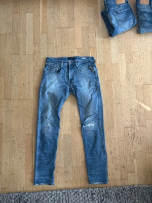 Replay anbass jeans - Säljer ett par blå jeans från Replay med snygga slitningar och tvättade detaljer. Modellen har smal passform, klassiska fem fickor och dragkedjegylf. Perfekta för dig som gillar en avslappnad men trendig stil.