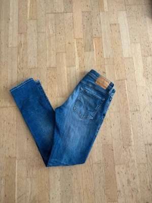 Jack&jones slim fit Glenn - Säljer ett par blå slim fit jeans med snygga tvättade detaljer och klassisk femficksmodell. Jeansen har en skinnpatch bak i midjan och smal passform hela vägen ner. Perfekta för en avslappnad och trendig look. OBS! har ett litet hål i sig därav priset 