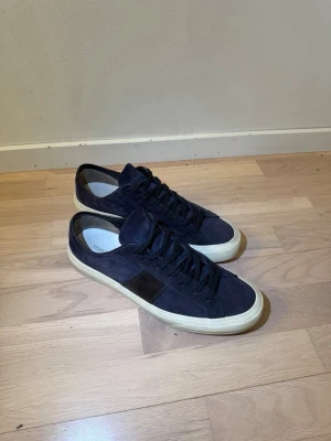 Mörkblå sneakers från Tom Ford - Snygga mörkblå sneakers från Tom Ford i mocka med svarta detaljer och vit sula. Klassisk låg modell med rund tå och svarta skosnören. Perfekta för en stilren och trendig look. 