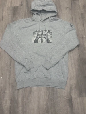 Valient hoodie  - Snygg grå hoodie med huva och dragsnören. På bröstet finns ett svartvitt tryck av en bro med coola detaljer. Hoodien har ribbade muddar vid ärmar och midja.