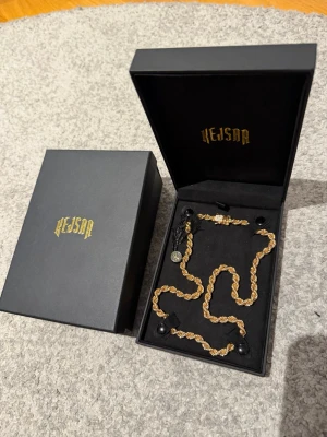 Guldfärgat Cordell -halsband från Kejsar - Säljer ett snyggt guldfärgat halsband från Kejsar med repkedje-design. Halsbandet har en tvinnad form som ger en exklusiv känsla och kommer i en elegant svart ask med guldfärgad logga. Perfekt accessoar för att lyfta din stim, kedjan är en cordell kedja med 6mm bredd och 55cm längd har ett kistlås som håller bra och har stenar på sig, kedjan är använd max 5 gånger och är fortfarande i helt nytt skick och fortfarande lika glänsig som den först var vid köp. Pris kan diskuteras de är bara att skriv