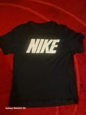 Svart Nike t-shirt med stor logga - Snygg svart t-shirt från Nike med stor vit logga över bröstet. Klassisk passform och rund halsringning, perfekt till jeans eller shorts. Tillverkad i mjuk bomull för skön känsla hela dagen.