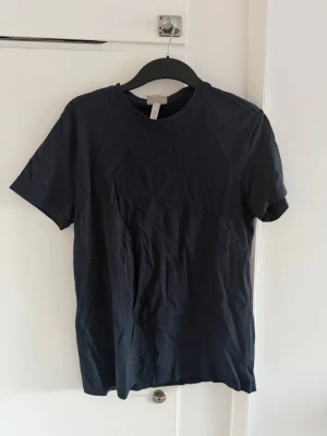 Svart basic t-shirt i bomull - En stilren svart t-shirt i mjuk bomull med rund hals och korta ärmar. Perfekt till jeans eller shorts för en enkel och clean look. Passformen är normal och tyget är slätt utan mönster eller tryck.