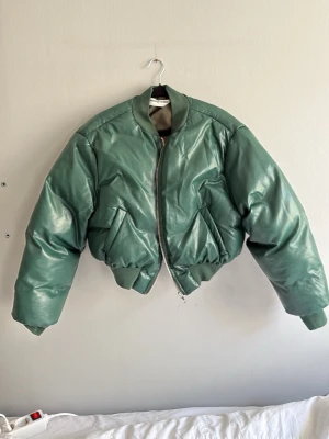 Grön oversized bomberjacka - Snygg grön bomberjacka i oversized modell med glansig finish. Jackan har dragkedja framtill, två sidofickor och ribbade muddar vid ärmslut och midja. Perfekt för dig som vill sticka ut med en trendig och cool look.