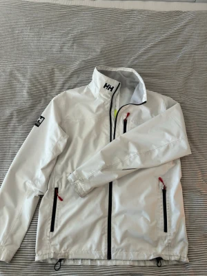 Vit vindjacka från Helly Hansen - Sjukt snygg vit vindjacka från Helly Hansen med svarta dragkedjor och röda detaljer. Perfekt nu inför skolstarten och när vädret börjar bli lite kyligare. Nypris på 1600kr!! Hör av er vid eventuella funderingar!