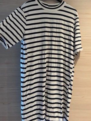 Randig t-shirtklänning från Bik Bok - Vit och svart randig t-shirtklänning från Bik Bok i supermjukt och elastiskt material. Avslappnad passform. 