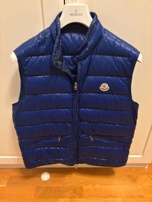 Blå Gui väst från Moncler - Schysst blå gui väst ifrån Moncler, såklart äkta, köpt för ungefär för 1 eller 2 år sen ifrån Sicuro Fashion, äkthetsbevis finns! I topp sick förutom dragkedjan som är lite lös men inget problem vid användning o går även att byta hos Moncler eller en kemtvätt. I storlek 5 men sitter liten i storlek så passar L mer.