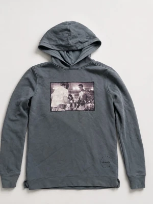 Grå hoodie med boxningsmotiv - Snygg grå hoodie med huva och ett stort svartvitt tryck på bröstet som visar en klassisk boxningsscen. Hoodien har långa ärmar och ribbade muddar. Perfekt för dig som gillar sportiga och unika plagg med coola motiv. Märker jag skrev är inte märket på hoodien 