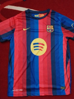 Barcelona matchtröja Lamine Yamal - Säljer en officiell FC Barcelona matchtröja från Nike med Lamine Yamal och nummer 10 på ryggen. Tröjan har blå och röda vertikala ränder, gul Nike-logga och Spotify som sponsor framtill. Tillverkad i Dri-FIT material för bästa komfort under träning eller match.