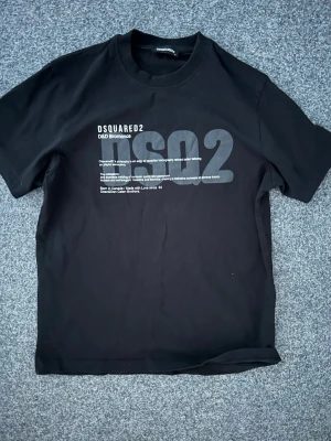 Svart Dsquared2 t-shirt med tryck - Säljer en svart t-shirt från Dsquared2 med stort tryck och text på bröstet. Klassisk rund hals och korta ärmar. Perfekt för dig som gillar streetwear och vill ha en stilren men ändå statement t-shirt. Påse och tag tillkommer!
