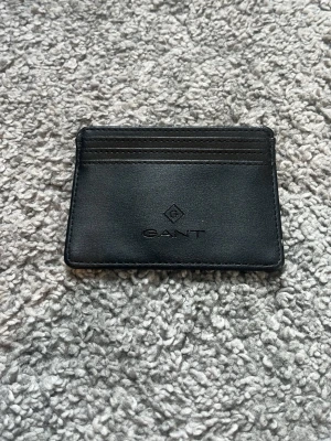 Svart kortfodral från GANT - Snyggt och stilrent svart kortfodral från GANT i äkta läder. Fodralet har flera kortfack på ena sidan och en slät baksida. Perfekt för dig som vill ha ett smidigt och klassiskt sätt att bära dina kort. Har aldrig använt kortfodralet. Nypris 800, mitt pris 400