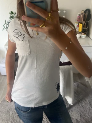 Vit t-shirt med tryck och ficka - Vit t-shirt i bomull med korta ärmar och en liten bröstficka. Tryck med texten 'You can't catch me!' vid fickan och ett litet motiv nertill. Perfekt till jeans för en avslappnad look.