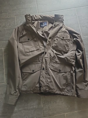 Olivgrön vindjacka från Bondelid - Snygg olivgrön vindjacka från Bondelid med fyra stora fickor framtill och knappar. Jackan har klassisk krage och är tillverkad i ett lätt, vindtätt material, perfekt nu till hösten för dig som vill ha en lite shysstare look. (Använd endest få tal gånger) ny pris 1799kr. 