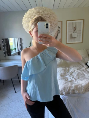 Ljusblå oneshoulder topp med volang - Säljer en superfin ljusblå one-shoulder topp🩵. Toppen har en fin volang och är ärmlös med en luftig och skön passform. Materialet är lätt och svalt, perfekt för varma dagar!✨ Skulle säga att den passar storlek S/M.